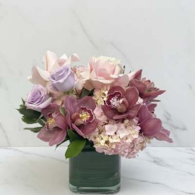 Pink and lavender flowers arranged in a square glass vase