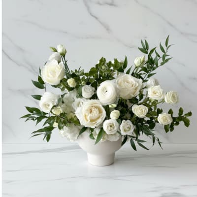 Low white arrangement of ivory roses and ranunculus in a white ceramic bowl