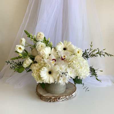 White floral arrangement in a ceramic vase with trailing greenery