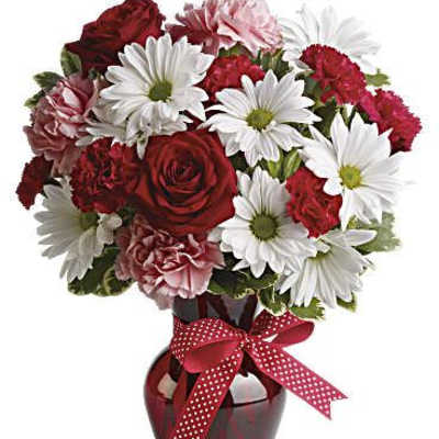 Bouquet of red roses, white daisies, and pink carnations in a red vase with ribbon