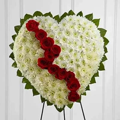 Heart-shaped floral tribute with white flowers and a diagonal line of red roses