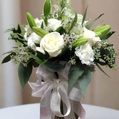 White roses and lilies arranged in a glass vase with a silver ribbon