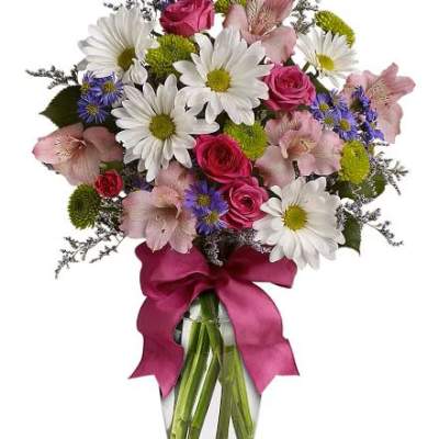 Mixed bouquet of white daisies, pink roses, and other blooms in a glass vase with a fuchsia ribbon bow