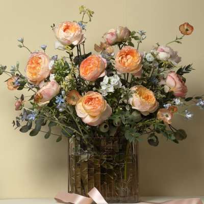 Peach roses and blue accent flowers in a clear glass vase