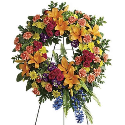 Colorful floral wreath on a black easel with orange lilies and mixed blooms