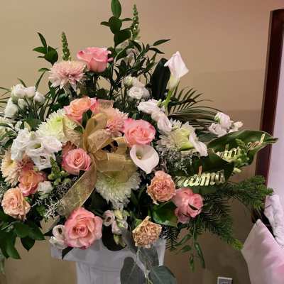 Large pink and white floral arrangement with a gold ribbon in a white pedestal vase