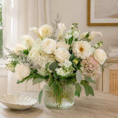 White floral arrangement in a clear glass vase with roses and calla lilies