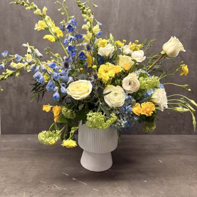 Blue and yellow mixed flower arrangement in a white vase