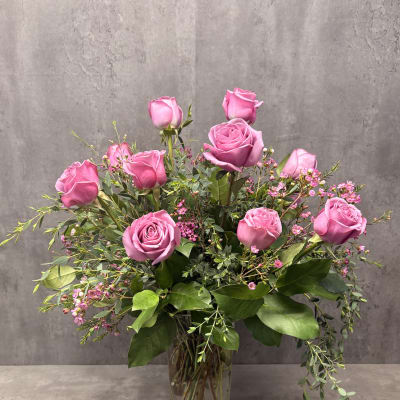 Pink roses arranged in a clear glass vase with small pink filler flowers.