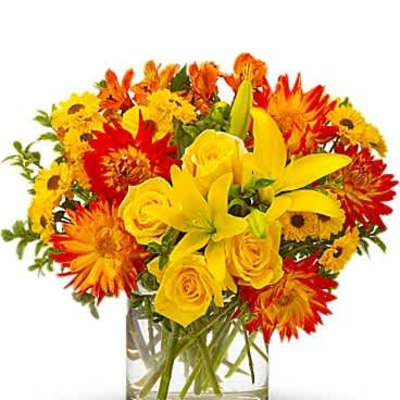 Short bouquet of yellow lilies, yellow roses, and orange mums in a clear glass vase