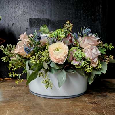Low floral arrangement in a white container with pale roses and mixed blooms