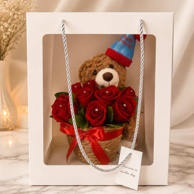 Teddy bear in a gift box with red roses and a birthday hat