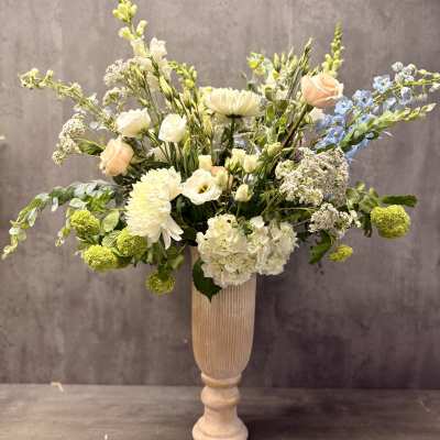 Tall floral arrangement in a pedestal vase with white, peach, and blue blooms