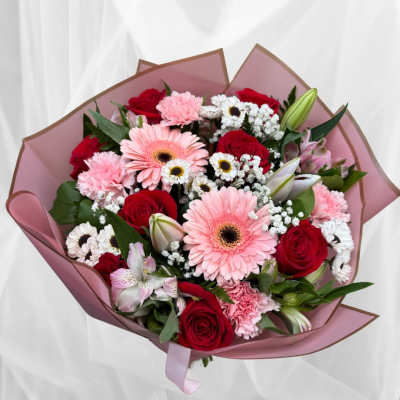 Hand-tied bouquet of pink gerberas, red roses, and mixed white blooms wrapped in pink paper