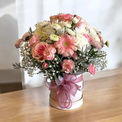 Pink and white mixed flower arrangement in a round hatbox with a pink ribbon