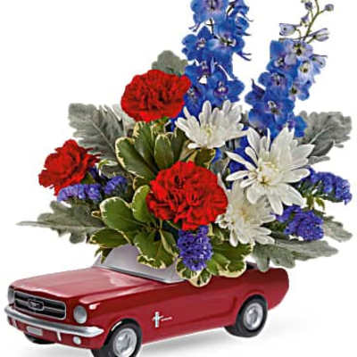 Floral arrangement in a red toy car container with red, white, and blue flowers