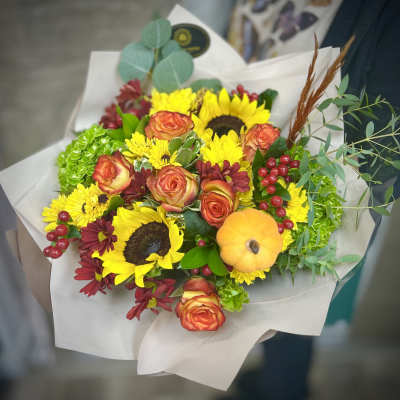 Autumn bouquet with sunflowers, orange roses, yellow mums and a small decorative pumpkin in paper wrap