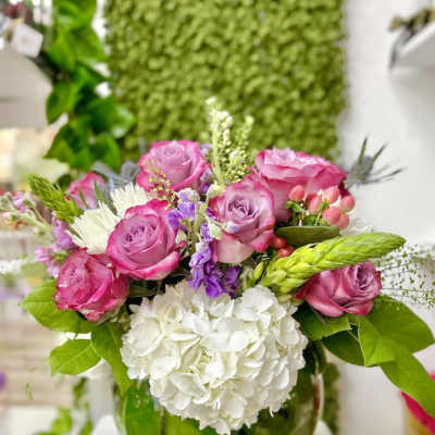 Low glass vase of pink roses and mixed blooms arranged above white hydrangeas