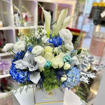 Box arrangement of white calla lilies, roses, and blue hydrangeas with silver accents in a white square container