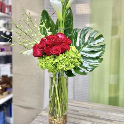 Tall arrangement of white calla lilies, red roses, and green hydrangeas in a clear glass cylinder vase