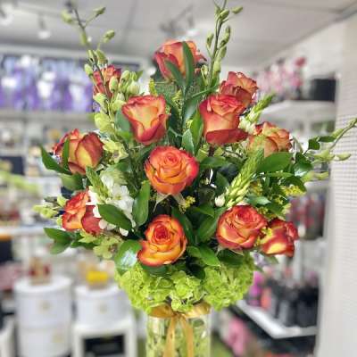 Tall arrangement of orange and yellow roses with green hydrangeas in a clear glass vase