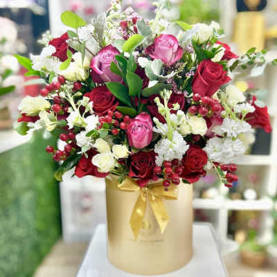 Large arrangement of red and pink roses with white flowers in a gold hatbox container