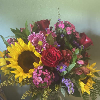 Bouquet of sunflowers, red roses, and pink mixed flowers in a glass vase
