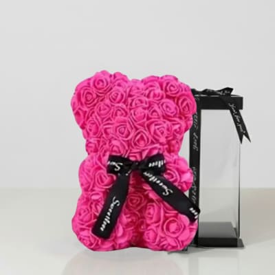 Pink rose teddy bear with a black ribbon beside a clear gift box