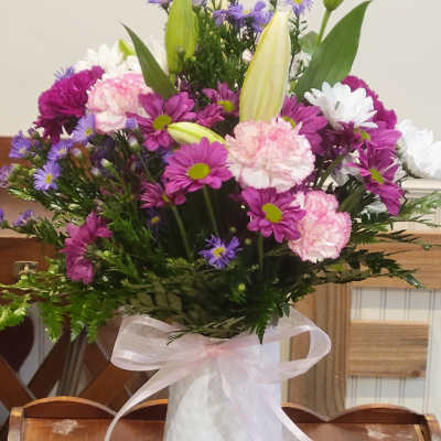 Mixed bouquet of lilies, daisies, and carnations in a white vase