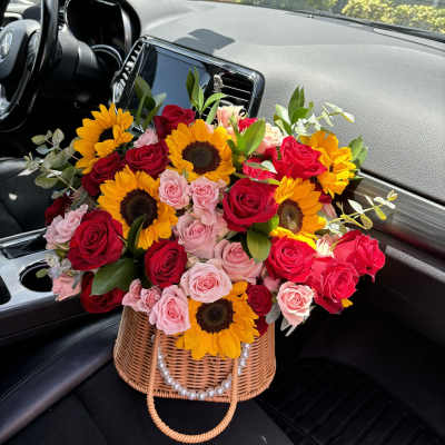 Basket arrangement of red and pink roses with sunflowers in a car seat