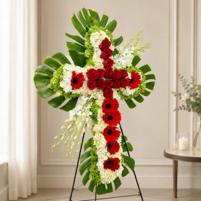 Cross-shaped floral standing tribute with red roses, white blooms, and green leaves