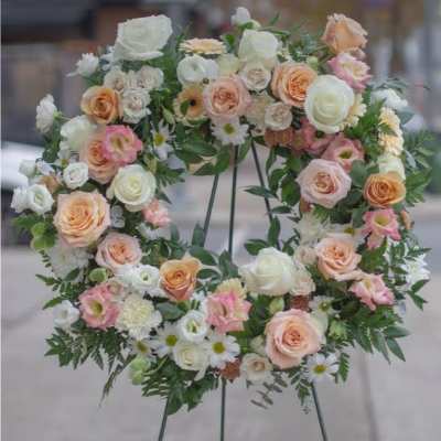 Circular floral wreath on a stand with white, peach, and pink blooms