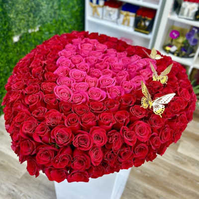 Large heart-shaped arrangement of red and hot pink roses on a white box with gold butterflies.