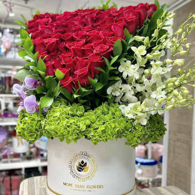 Tall hatbox arrangement of red roses, green hydrangeas, and white and purple orchids in a white box
