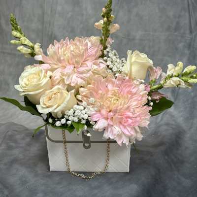 Pink and cream flowers arranged in a white gift box with a chain handle.