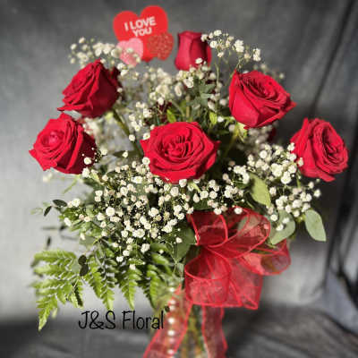 Red roses in a glass vase with baby's breath and a red ribbon