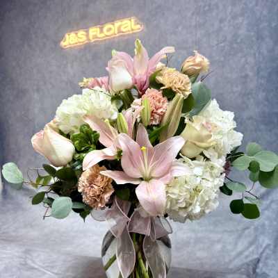 Pink lilies and white hydrangeas in a glass vase with a ribbon