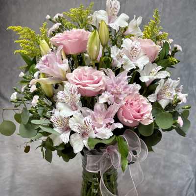 Pink roses and white lilies in a glass vase with a ribbon