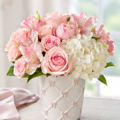 Pink roses and alstroemeria arranged in a white vase with pink bows