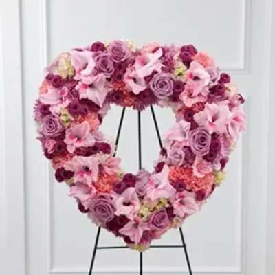 Heart-shaped floral wreath in pink and purple tones on a black stand