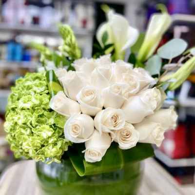 Round glass vase filled with white roses, white calla lilies, and green hydrangeas.