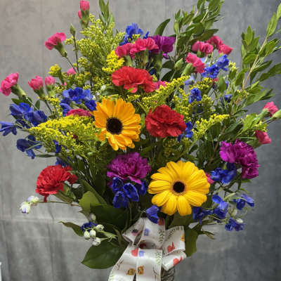 Mixed bouquet in a glass vase with yellow daisies, carnations, and blue flowers