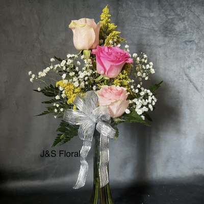 Pink roses and baby's breath in a glass vase with a silver bow