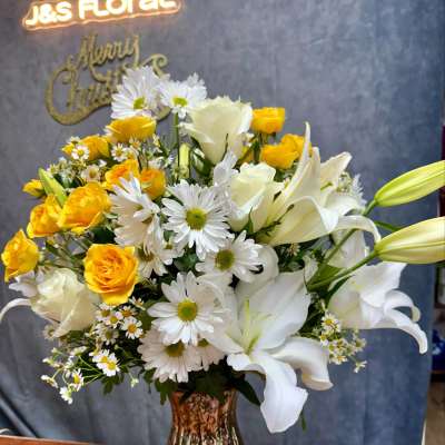 Yellow roses and white lilies in a glass vase with white daisies