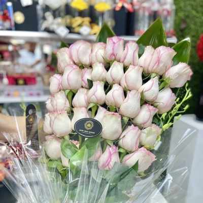 Tall bouquet of white roses with pink edges wrapped in clear cellophane with a black ribbon