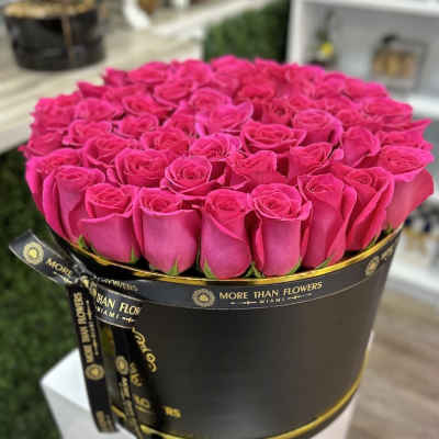 Round hatbox of bright pink roses in a black box with gold trim and ribbon