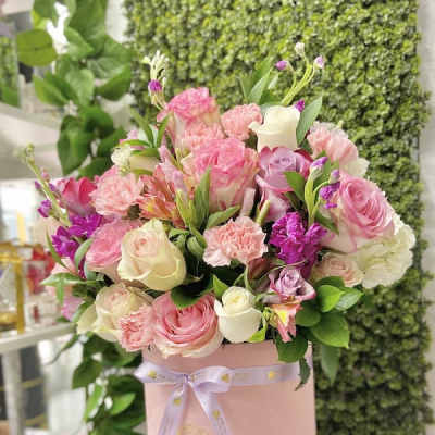 Round pink hatbox filled with pink, white, and purple mixed roses and carnations.