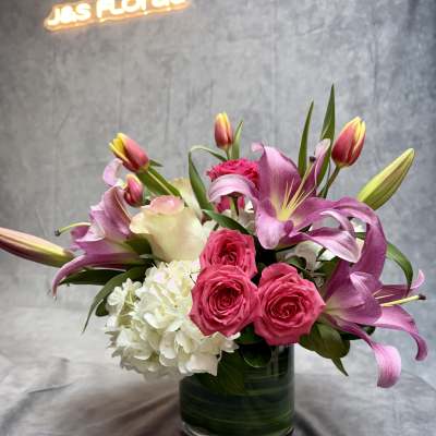 Pink lilies and roses arranged in a glass vase with white hydrangea.