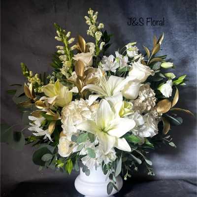 White floral arrangement in a white pedestal vase with gold foliage accents