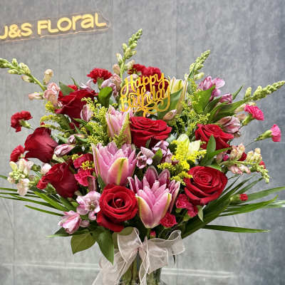 Bouquet of red roses and pink lilies in a glass vase with a birthday topper